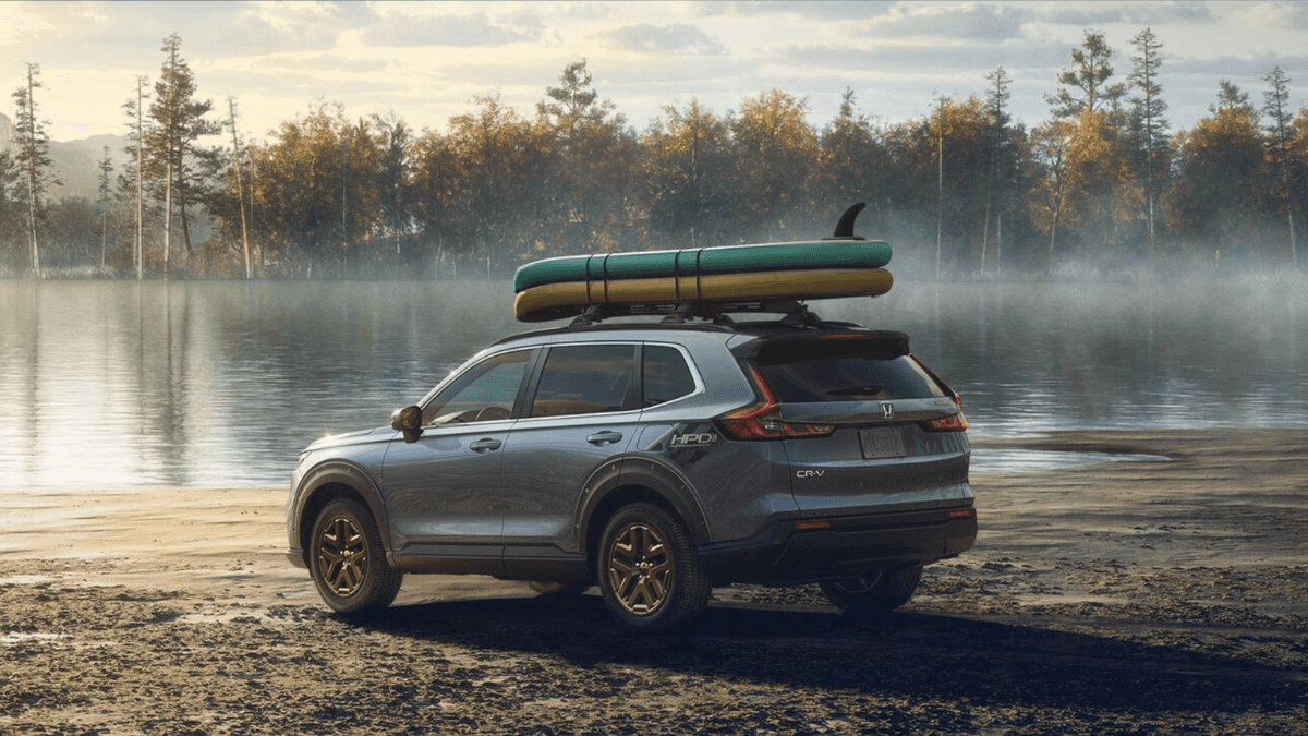 A side and rear view of the 2026 Honda CR-V parked in front of a body water with small boats fixed to the roof