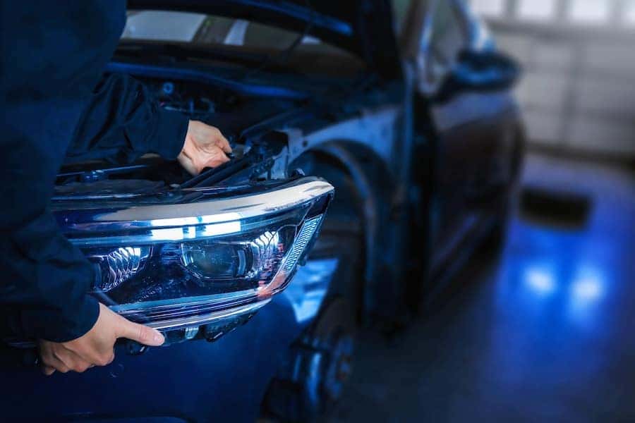 A service technician working on the headlights of a blue car