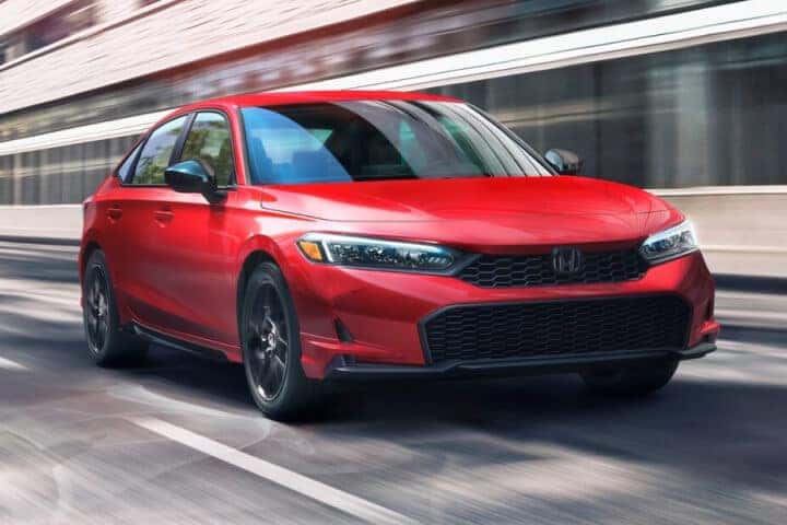 Three-quarter front shot of a 26 red Honda Civic Sport speeding along a modern city street