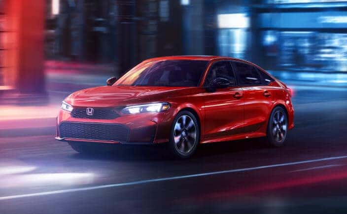 2026 Honda Civic Sedan Sport Touring Hybrid in rallye red, front three-quarter view driving through a neon-lit city at night.
