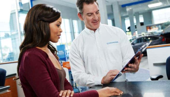 Honda representative reviews leasing and financing options with a customer at a dealership sales desk.