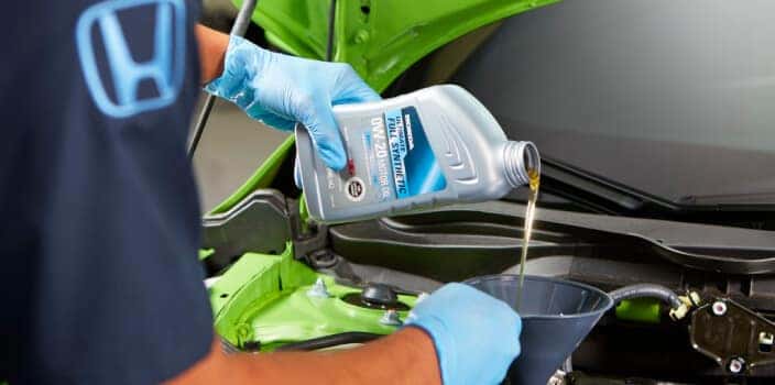  Honda technician pours full synthetic motor oil into an engine during routine maintenance.