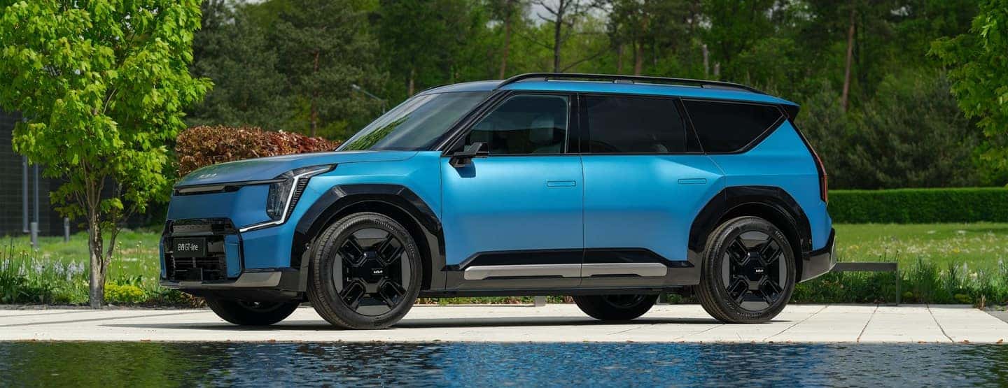 Blue 2024 Kia EV9 near water and trees. EV9 pricing launched.