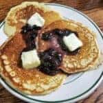 3 pancakes with butter and grape jelly on a white plate