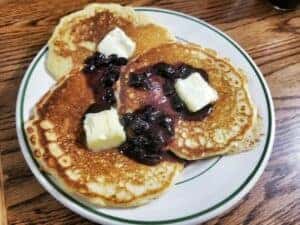 3 pancakes with butter and grape jelly on a white plate