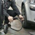 Man in Black Jacket and Black Pants Sitting Near Silver Vehicle while filling up tires