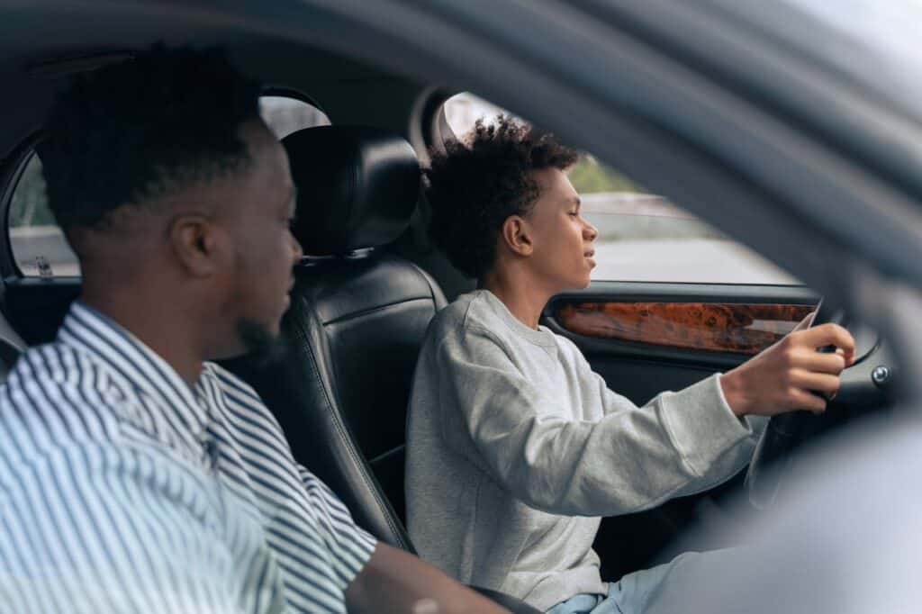 teenager driving car with another man instructing in passenger seat
