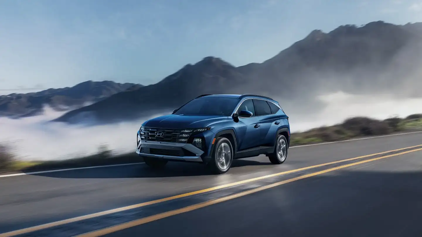 blue hyundai tucson suv driving on highway with mountains in background