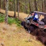 Man driving 4x4 utility vehicle up a muddy hill in forest