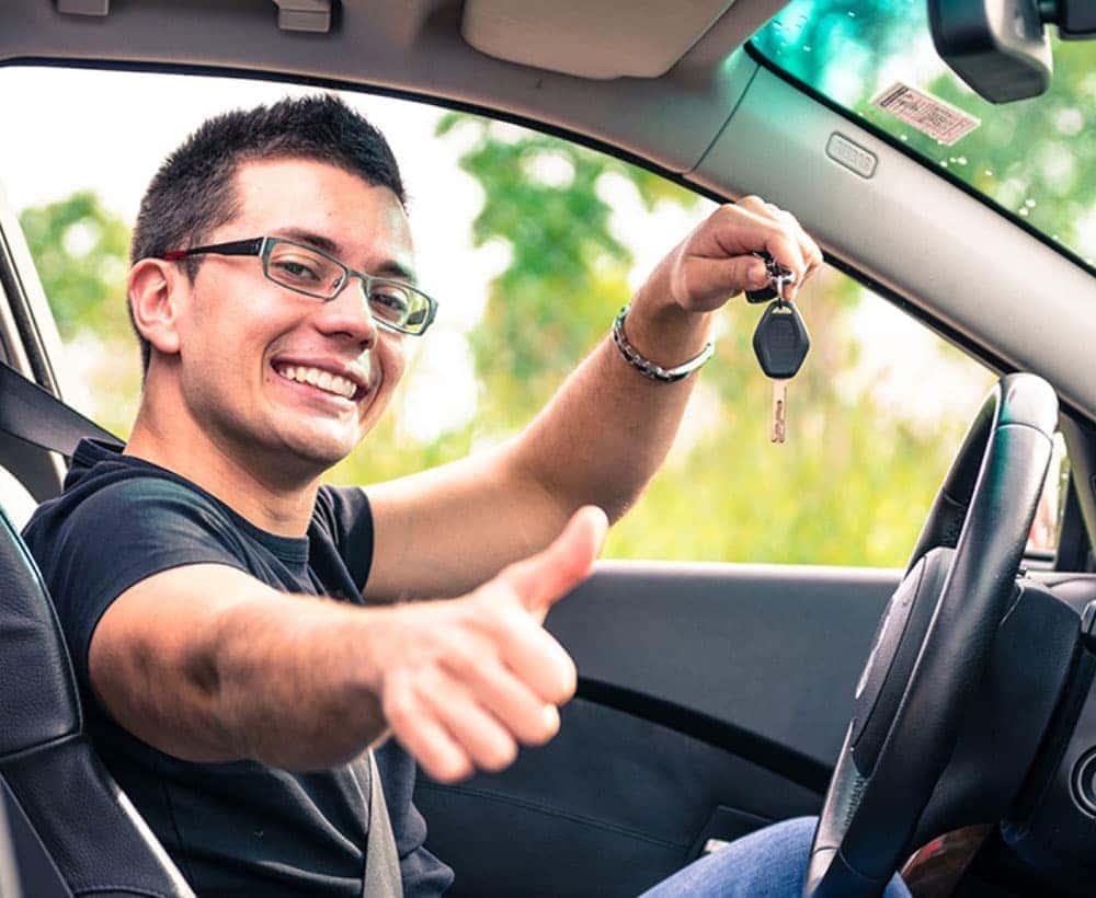 Man sitting in the driver's seat of a car holding his car keys up and giving a thumbs up