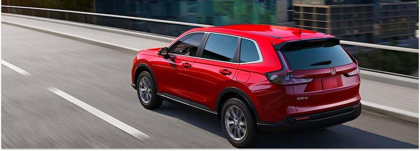 Red 2026 Honda CR-V EX SUV driving on a roadway in rear three-quarter view.