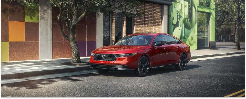 Front three-quarter view of a red 2026 Honda Accord sedan parked along a city street curb.