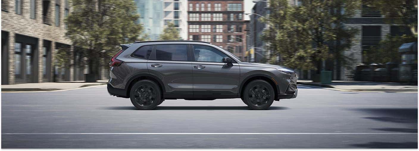 Side profile view of a gray 2026 Honda CR-V SUV driving on a city street.