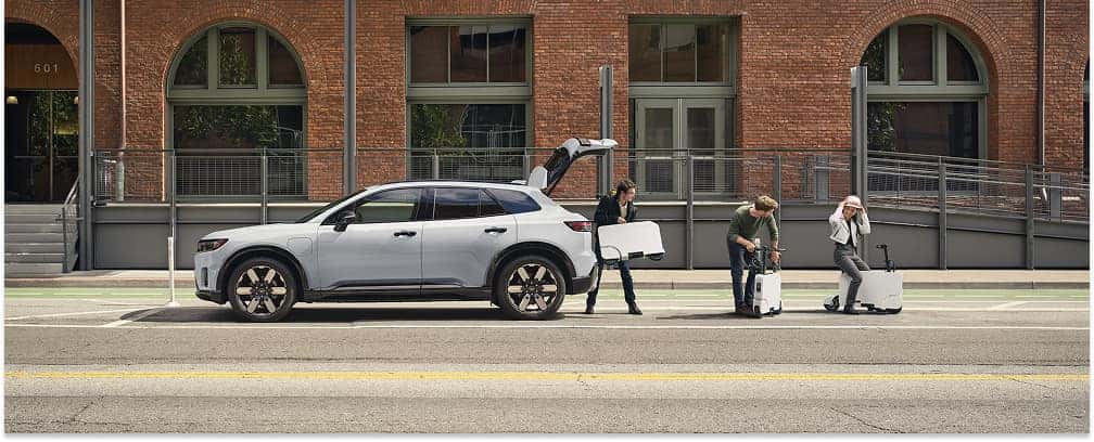 Side profile of a white 2026 Honda Prologue SUV parked on a city street with its tailgate open.