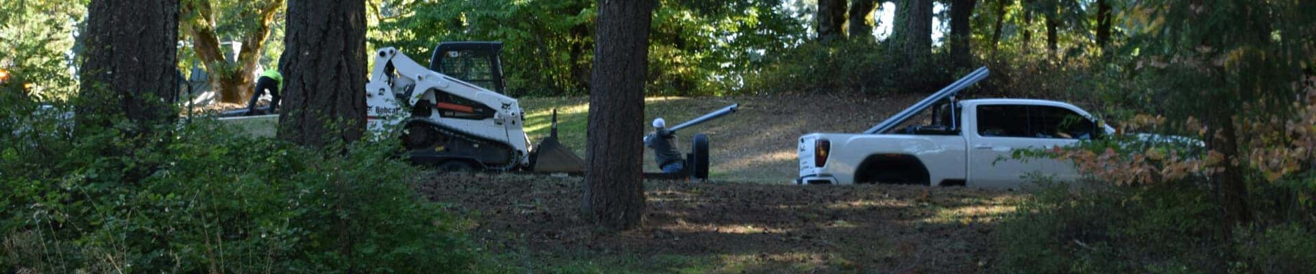 Side profile of a GMC Canyon AT4 in White carrying a steel pole on a wooded construction job.