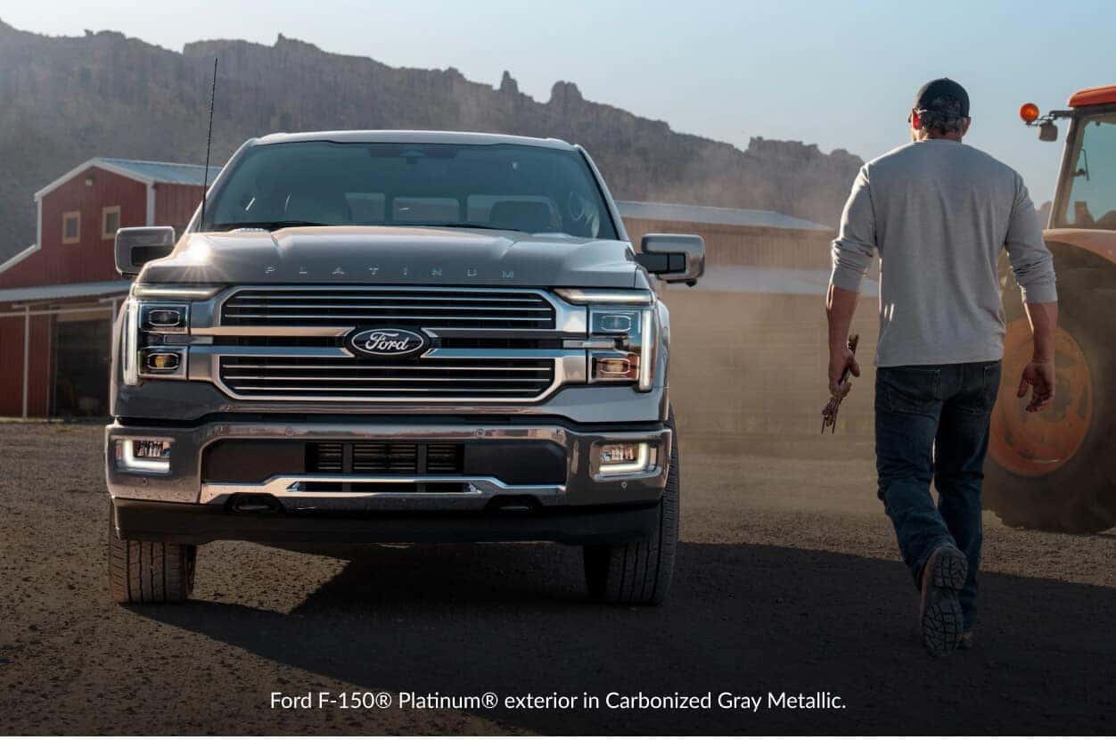 Front view of a Ford F-150 Platinum in Carbonized Gray on a ranch driveway as a worker walks toward.