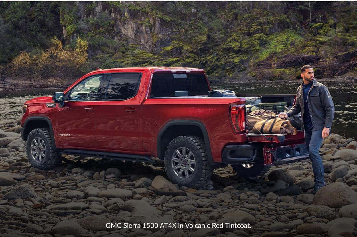 Rear three-quarter view of a GMC Sierra 1500 AT4X in Volcanic Red parked on a rocky bank.