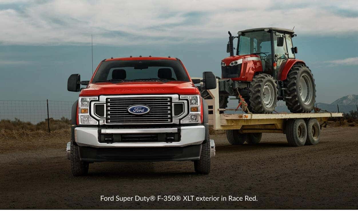 Front view of a red Ford F-350 Super Duty towing a red tractor on a flatbed trailer.