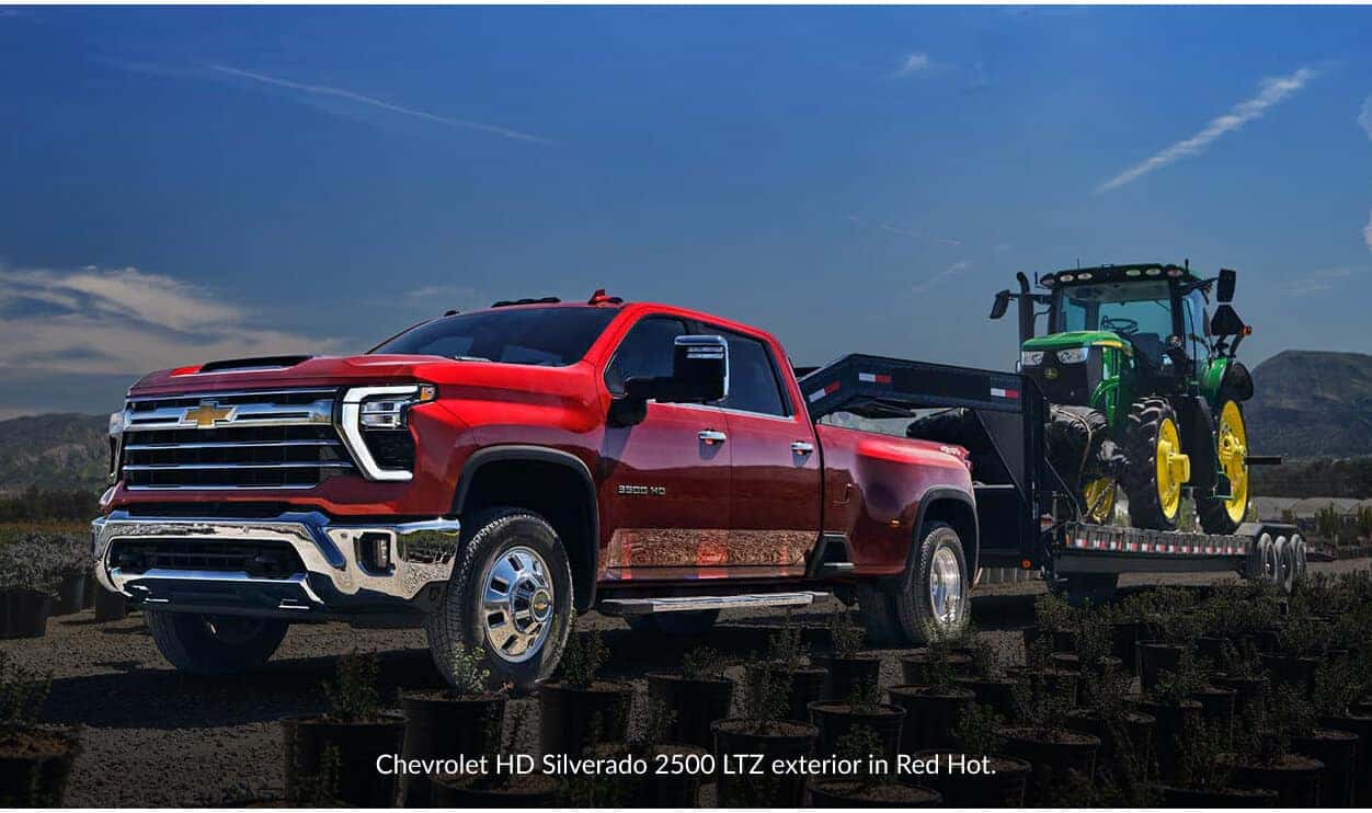 Front three-quarter view of a Chevrolet Silverado 2500 HD in Red Hot towing a green tractor.