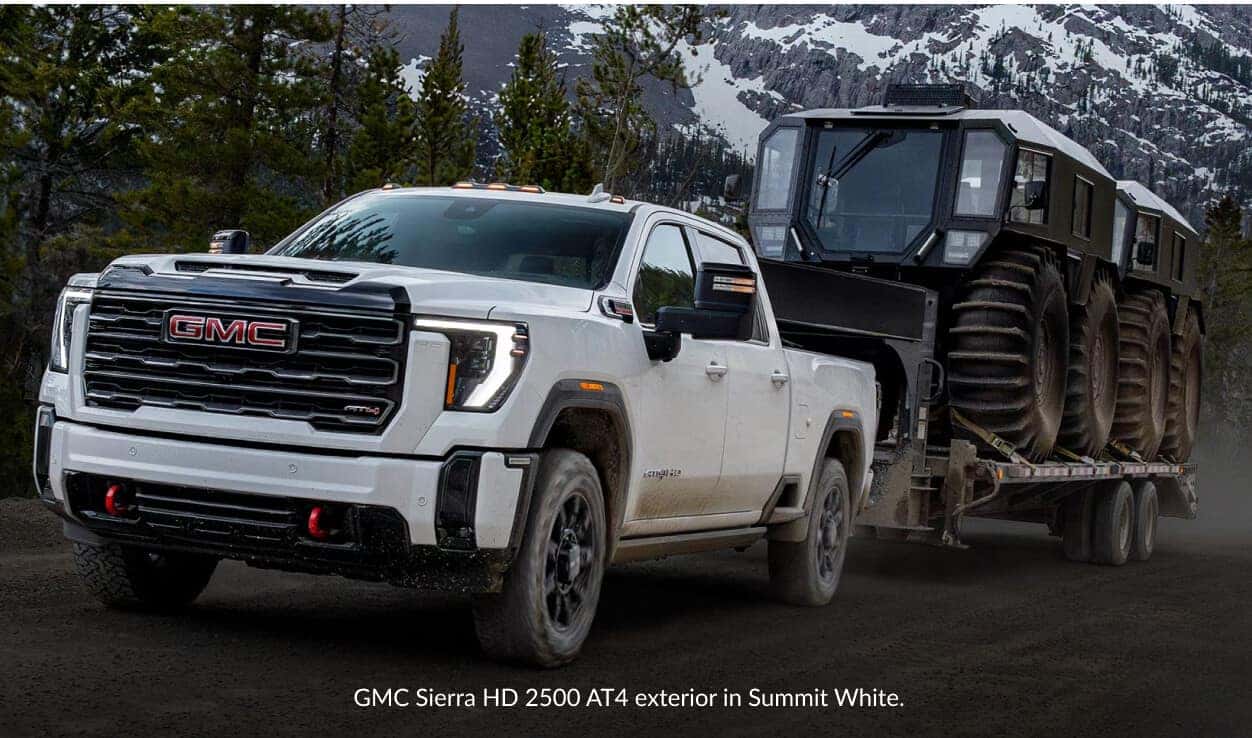 Front three-quarter view of a GMC Sierra 2500 HD AT4 in Summit White towing a vehicle.