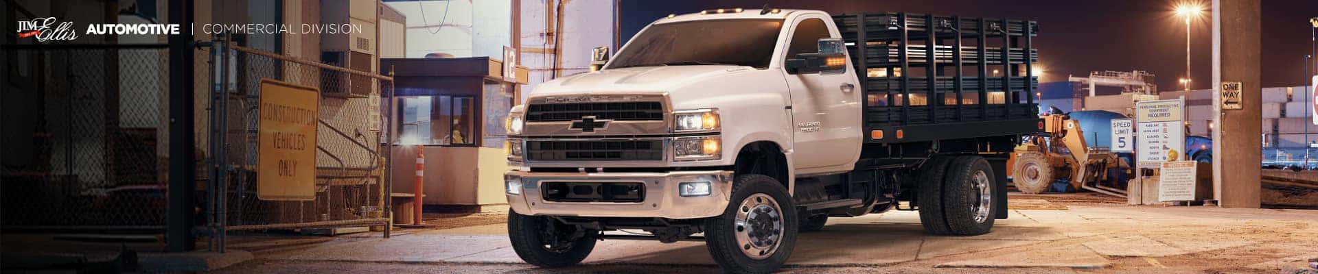 A Chevy flatbed utility truck parked in a commercial lot at night.
