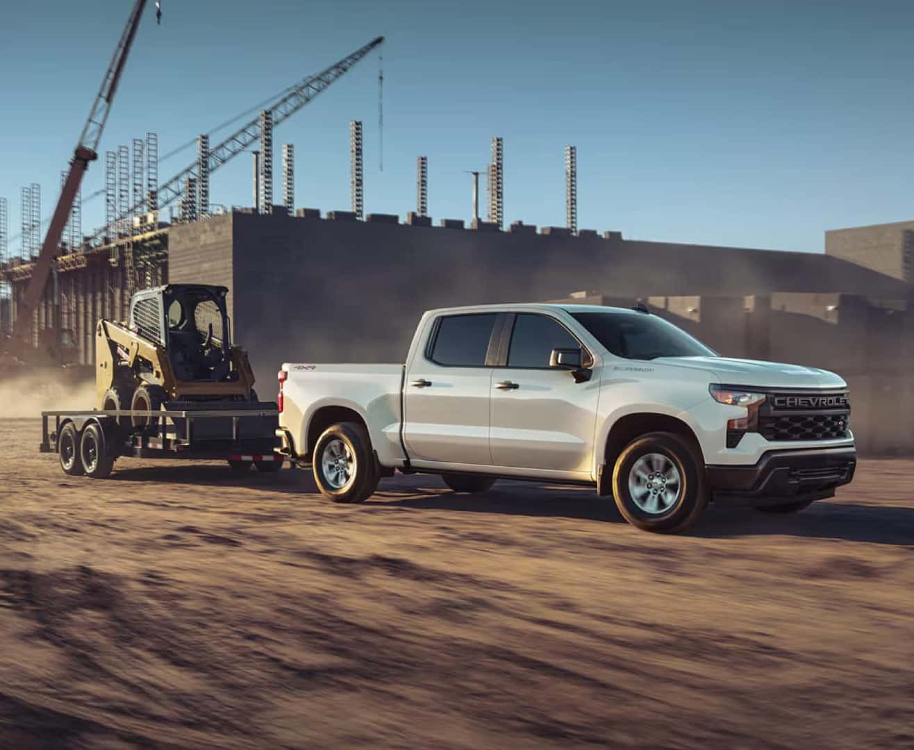 A silver Chevy pickup truck towing a forklift on a worksite.