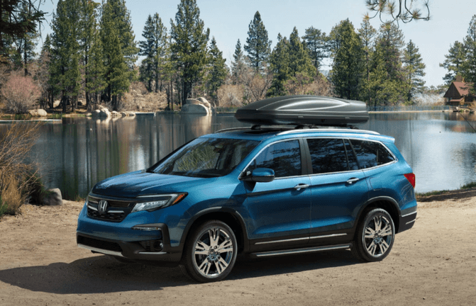 A blue Honda Pilot parked in front of a lake with cargo on the roof.