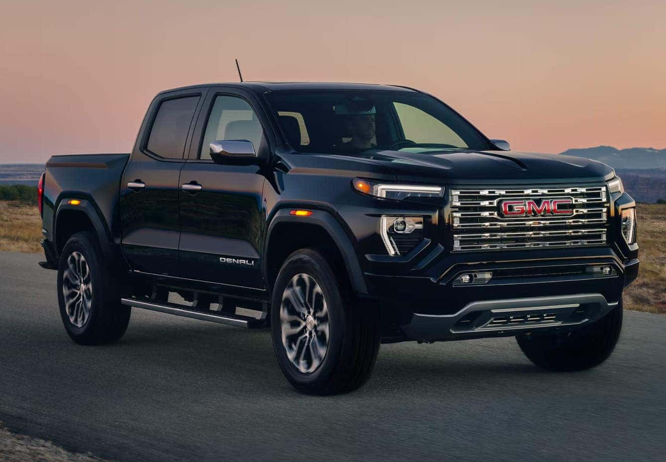 A sleek, black GMC pickup truck is parked on a road at sunset.
