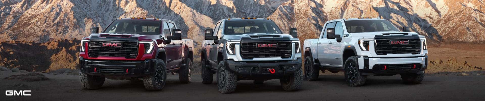 Front view lineup of three GMC Sierra 2500HD trucks including the AT4X and AT4X EV against a desert mountain.