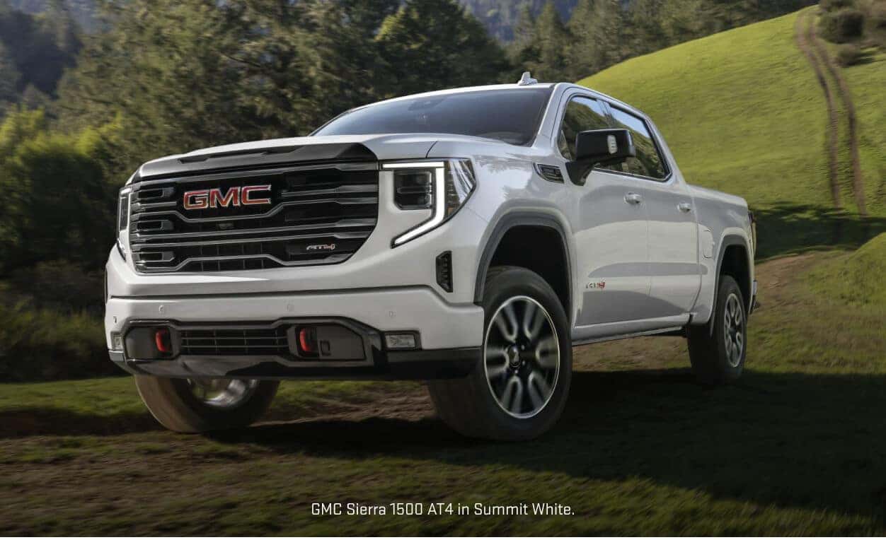 Front three-quarter view of a GMC Sierra 1500 AT4 in Summit White driving over a grassy mountain ridge.