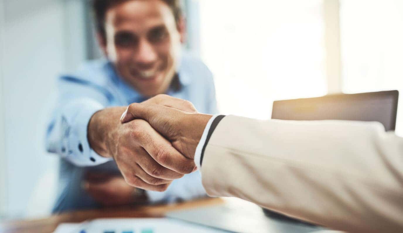 Customer and dealership representative shake hands while discussing financing and leasing options at a desk.