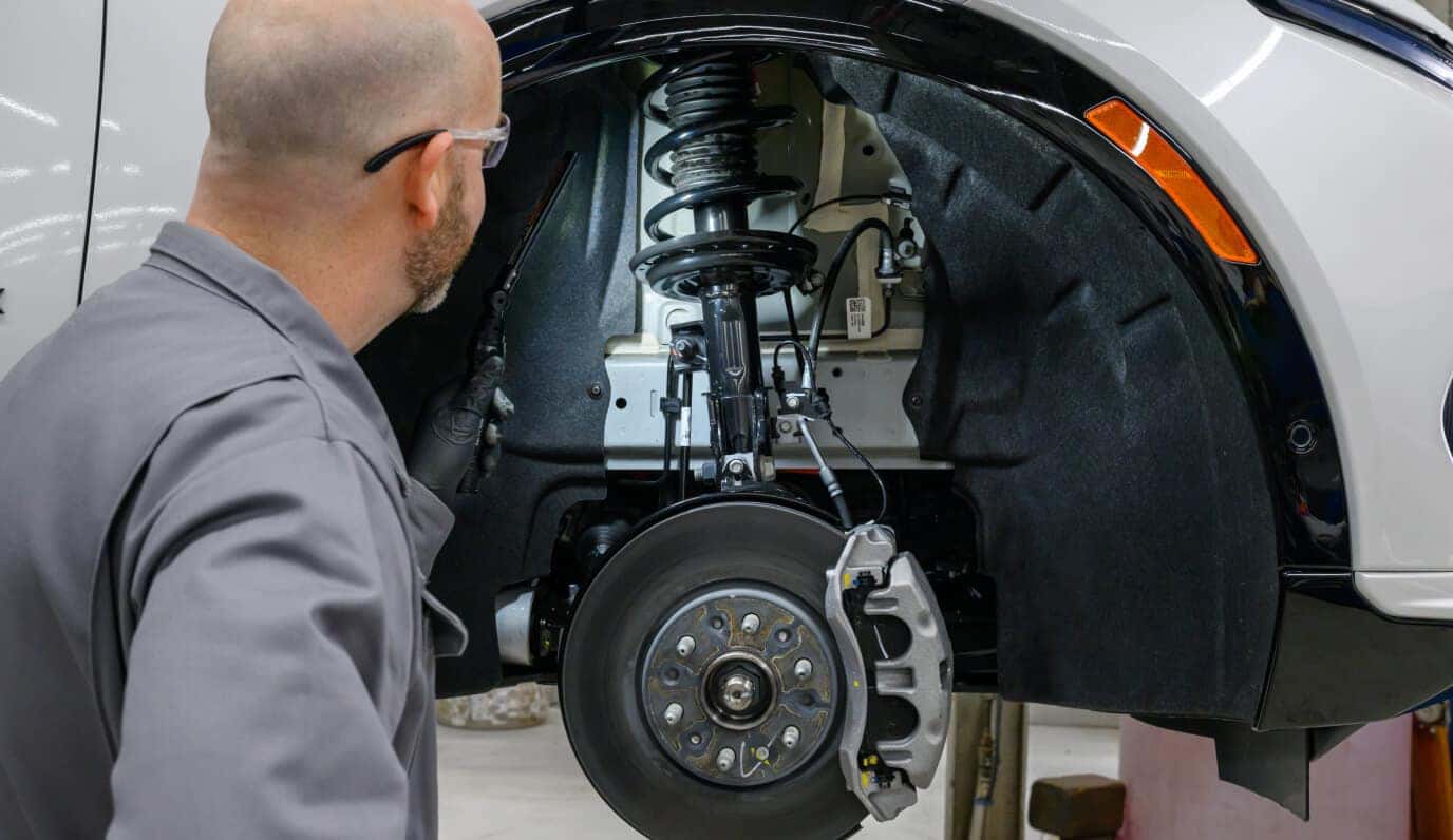 Certified GMC service technician inspects a vehicle’s front brake and suspension components with the wheel removed.