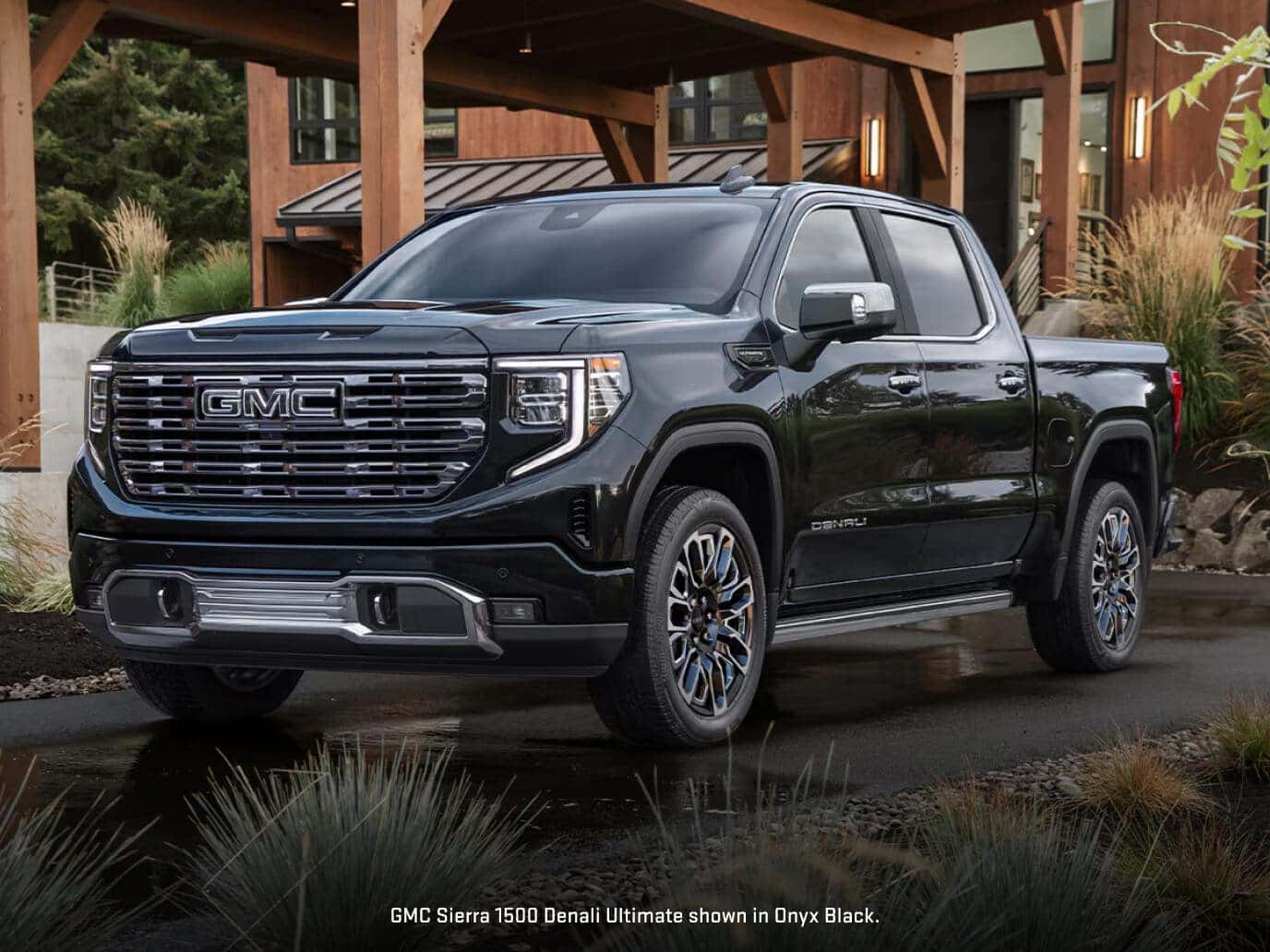 Front three-quarter view of a 2026 GMC Sierra 1500 Denali Ultimate in Onyx Black parked outside a modern timber-frame residential home.