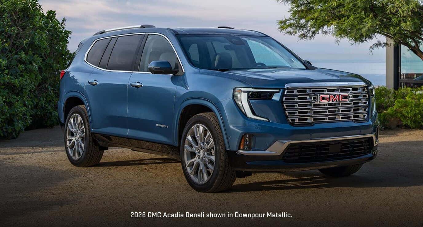 Front three-quarter view of a 2026 GMC Acadia Denali in Downpour Metallic parked along an coastal outlook with water in the background.