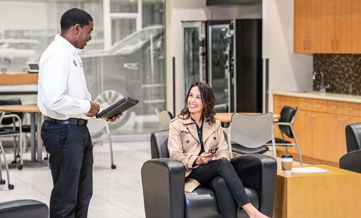 Candid view inside a GMC dealership customer lounge as an advisor with a tablet interacts with a client seated comfortably in a leather armchair.