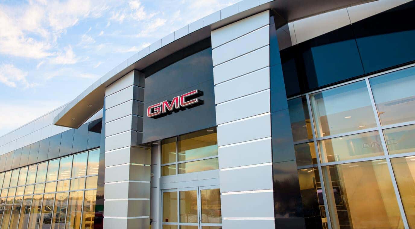 Low-angle exterior architectural view of a modern GMC dealership entrance featuring the prominent red GMC logo.