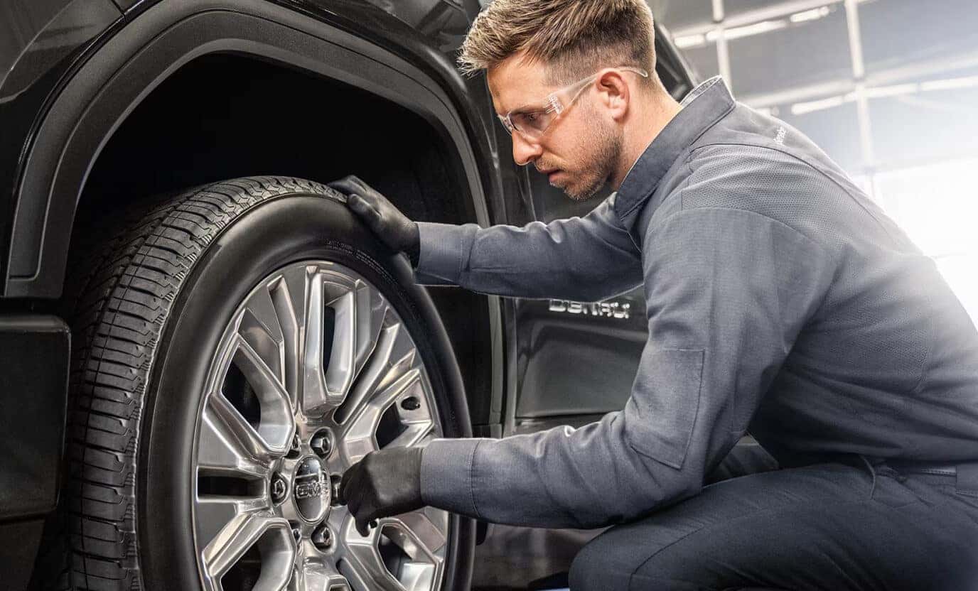 Close-up shot of a certified GMC technician wearing safety glasses inspecting a tire on a GMC Denali.