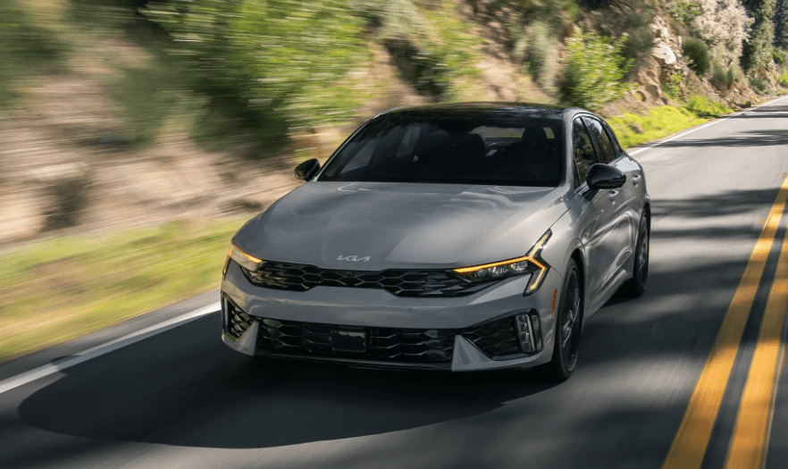 Stone colored 2026 Kia K5 zooming on road.