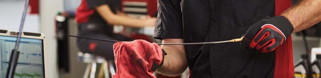 Difference between synthetic oil & conventional oil at Palmiero Toyota | Mechanic checking the oil dipstick of a car
