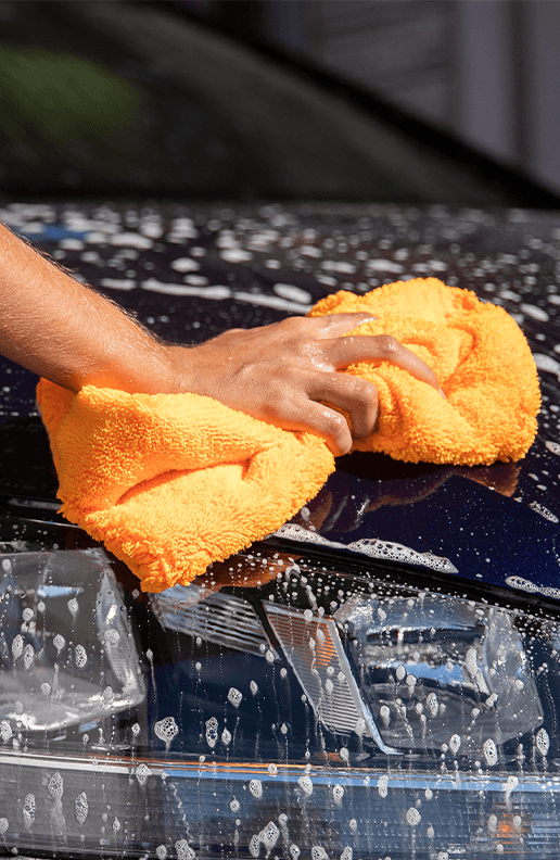 Accessories that help keep your Toyota protected at Palmiero Toyota in Meadville, PA | Person using an orange sponge to clean the soap on his car