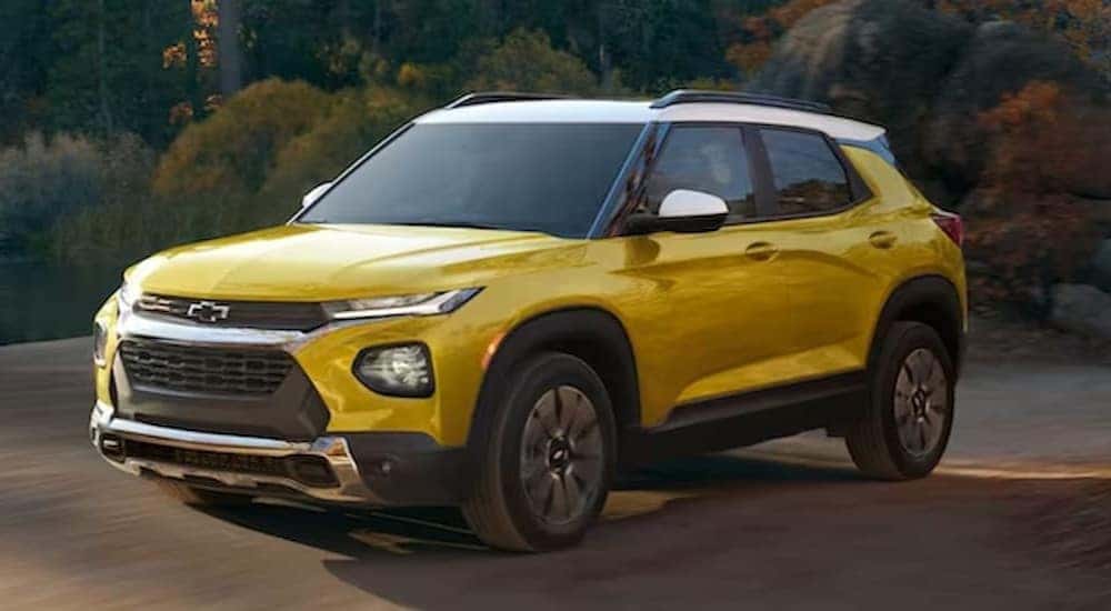A yellow and white 2023 Chevy Trailblazer is shown driving on a dirt road.