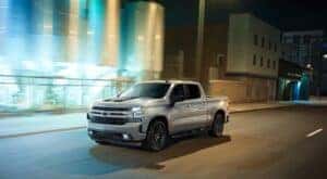A silver 2020 Chevy Silverado 1500 RST Rally Edition is shown driving on a city street at night.