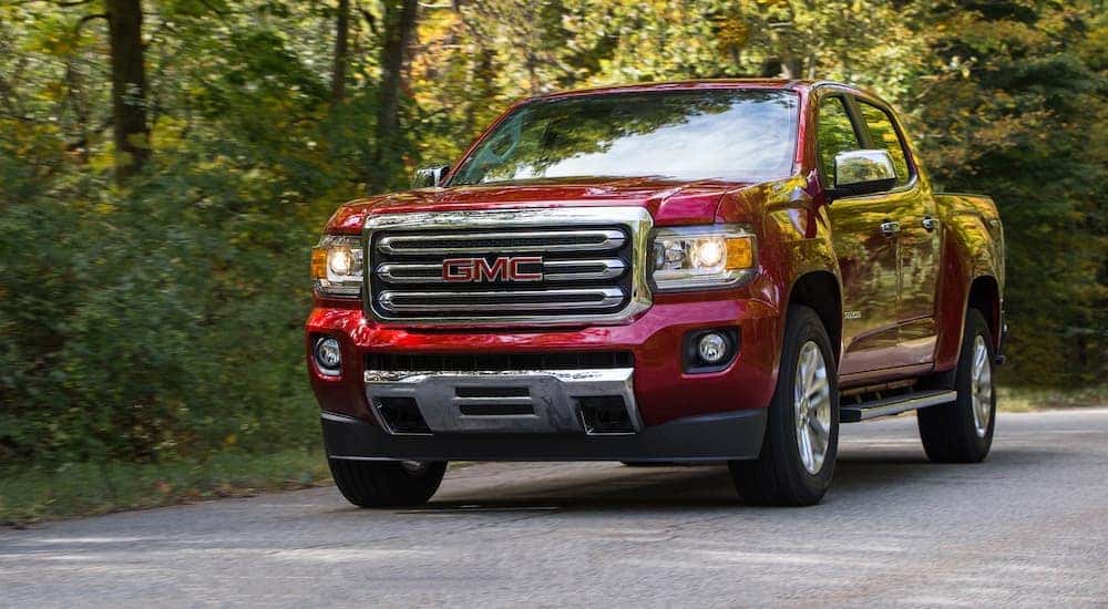 A red 2019 GMC Canyon SLT is shown driving on a tree-line road.