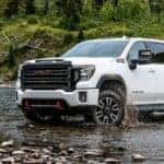 A white 2020 GMC Sierra 2500 HD AT4 is shown driving through a creek after looking for used GMC trucks for sale.