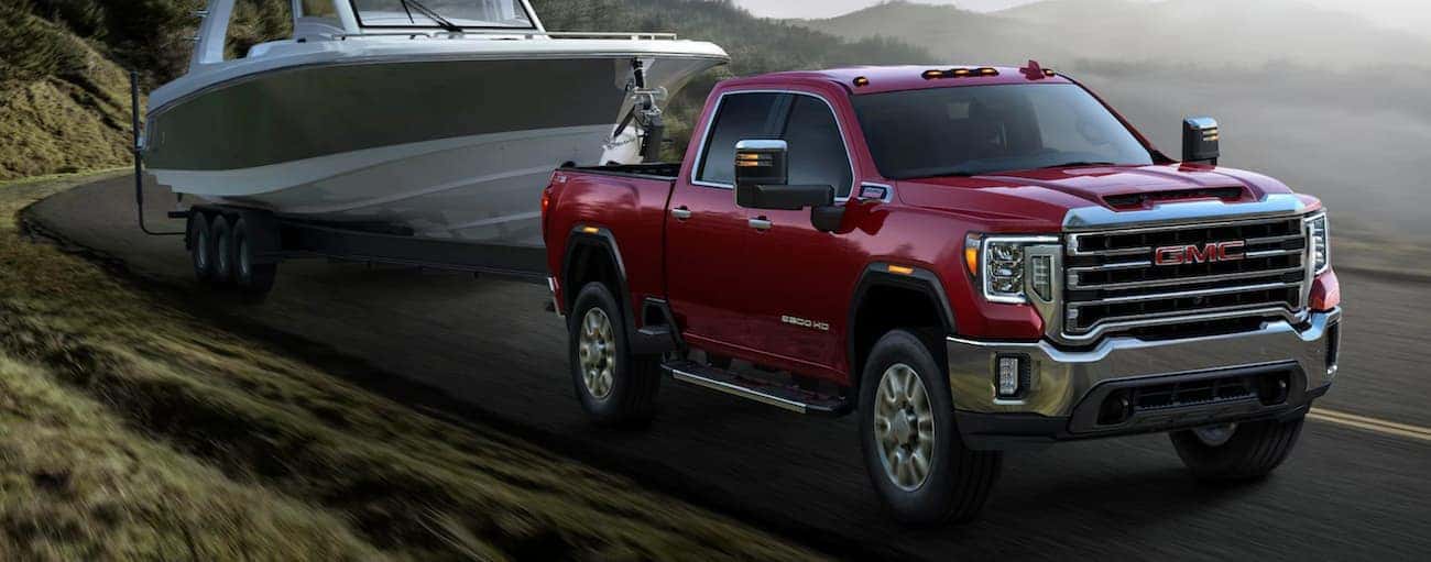 A red 2020 GMC Sierra 2500 HD is shown towing a boat next to a lake.