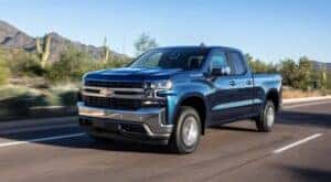 A blue 2019 Chevy Silverado 1500 is shown driving on a highway to view used trucks for sale.