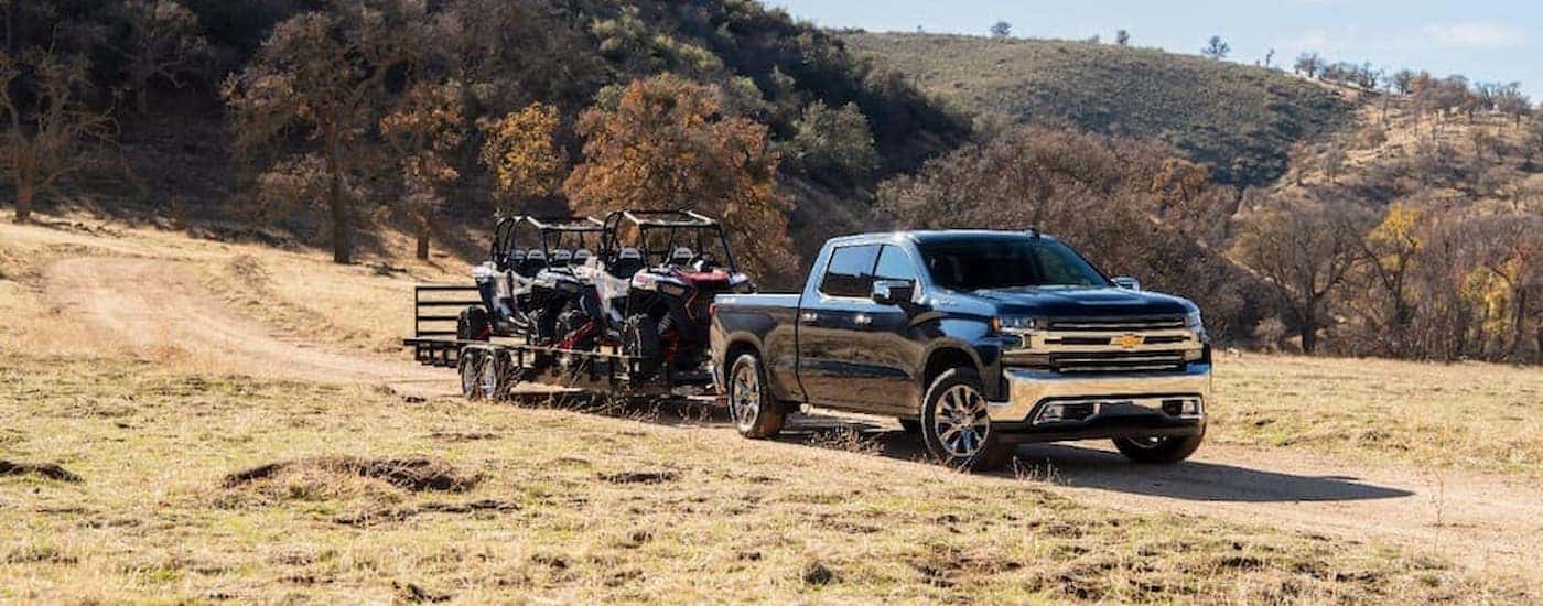 A black used 2020 Chevy Silverado 1500 for sale is shown towing an ATV through a field.