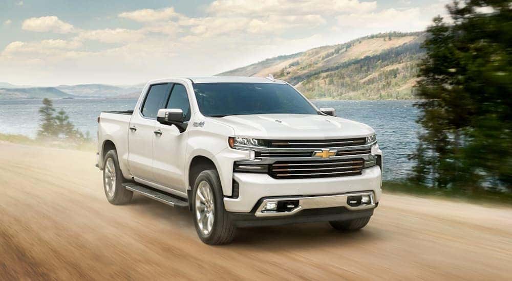 A white 2020 Chevy Silverado 1500 High Country is shown driving past a lake.