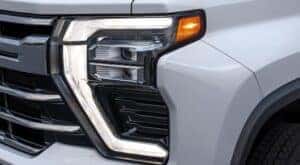 A close up of the headlight on a white 2024 Chevy Silverado 3500HD for sale is shown.