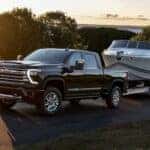 A black 2024 Chevy Silverado 3500 HD High Country is shown towing a boat.